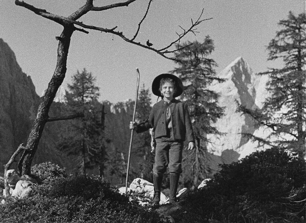 Kekec pod gorami in s palico v roki.